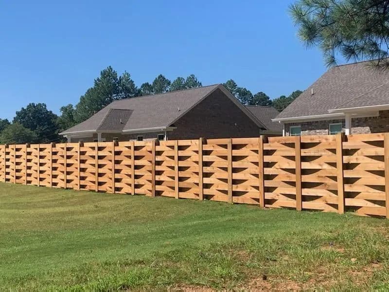 Long horizontal-board basketweave cedar fence running along a green lawn in front of brick homes
