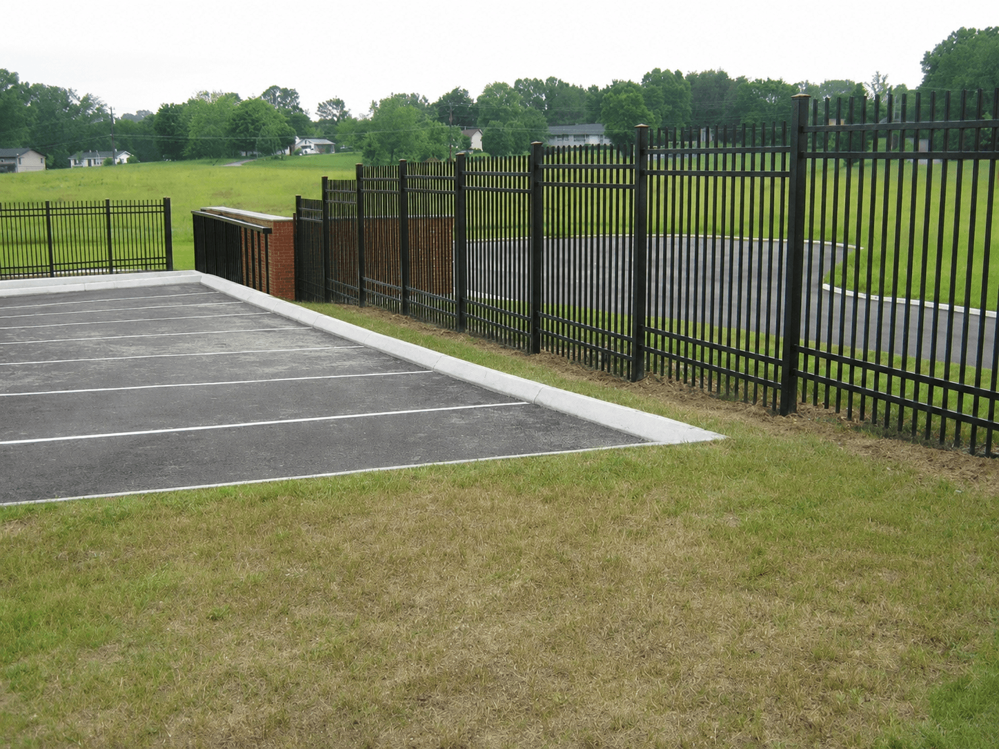 A black ornamental steel security fence along a commercial parking lot with a brick screen wall