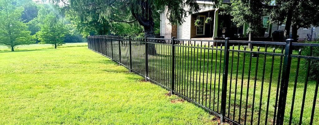 A black ornamental aluminum fence running along a green lawn beside a two-story home