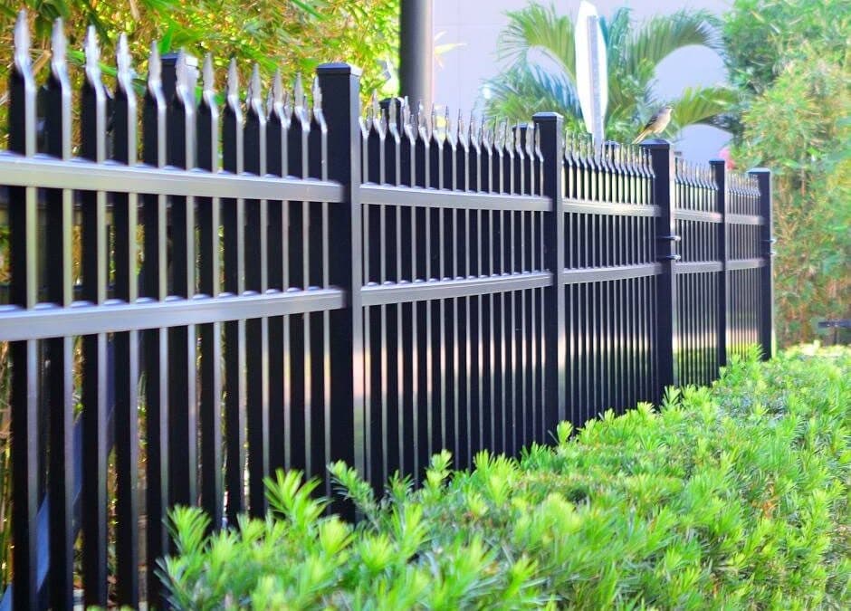 A black ornamental aluminum fence with spear-top finials running alongside lush green hedges