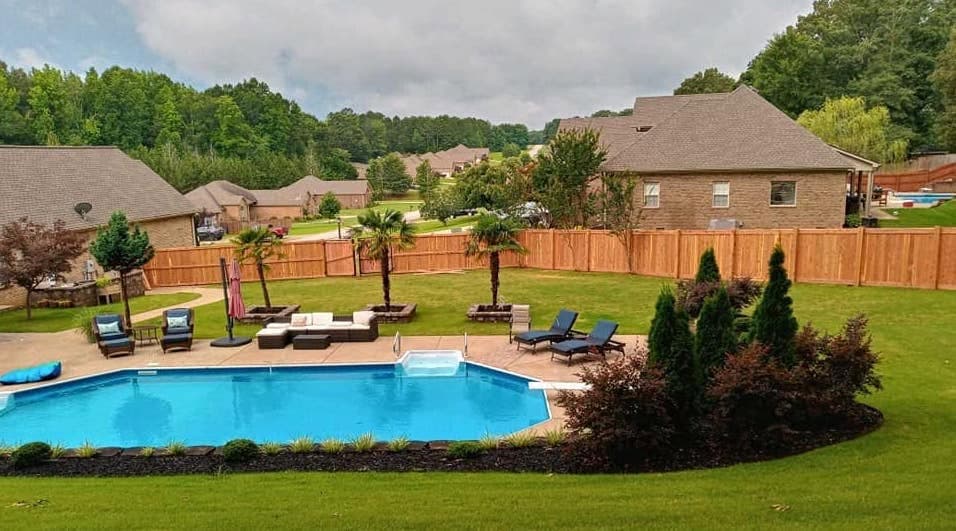 A cedar wood privacy fence enclosing a backyard with an in-ground pool, patio, and landscaping