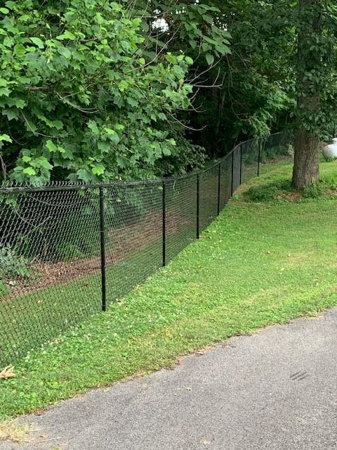 Photo of chain link metal fencing that runs through a heavily treed and natural area. The fencing is black.