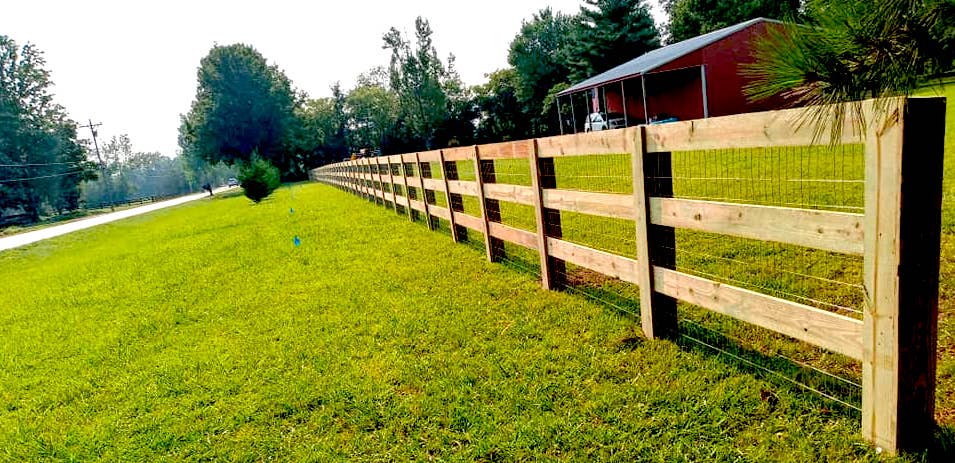Photo of wood slat fence with mesh wire. The fence protects a property along a roadway