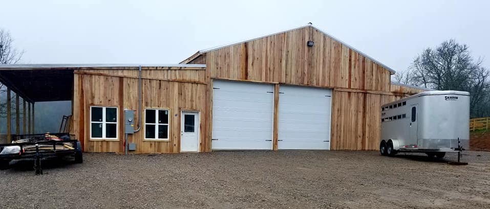 Photo of enclosed wood barn. Sliding doors form the entry. The vertical boards are a striking change from the traditional horizontal board barn construction. Wood framed squares spaced along the front and sides of the barn with wooden "X" desgins in the squares give the appearance of windows. A large star of David above the sliding doors is outlined in wood at the hayloft height. Wood lattice trim deliniates the support header over the sliding doors. The barn is energized with a large security light over the barn doors and the rear of the barn sports a stone chimney.