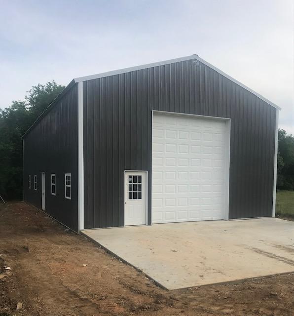Photo of exterior of horse barn with 2-story tractor door and standard entrance, side windows and doors and a-frame structure. The outbuilding is made of metal siding