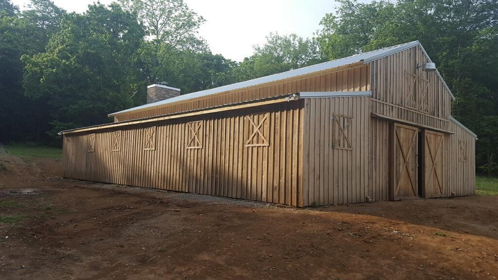 Photo of enclosed wood barn. Sliding doors form the entry. The vertical boards are a striking change from the traditional horizontal board barn construction. Wood framed squares spaced along the front and sides of the barn with wooden "X" desgins in the squares give the appearance of windows. A large star of David above the sliding doors is outlined in wood at the hayloft height. Wood lattice trim deliniates the support header over the sliding doors. The barn is energized with a large security light over the barn doors and the rear of the barn sports a stone chimney.