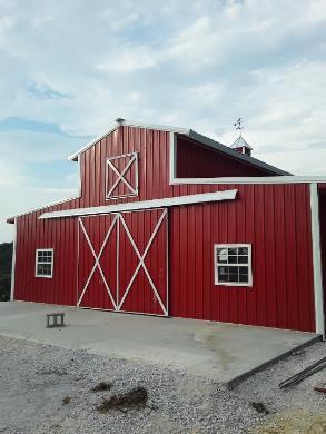 Photo of a red barn with sliding barn doors flanked by windows and a hayloft "door" above the sliding doors. A jaunty weathervane can be seen at the far end of the barn.